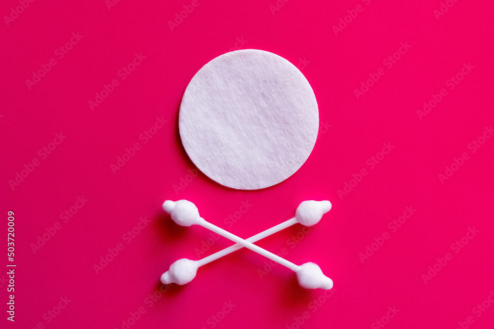 crossed ear sticks under white cotton pad on pink background, top view. crossed ear sticks under white cotton pad on pink background, top view.