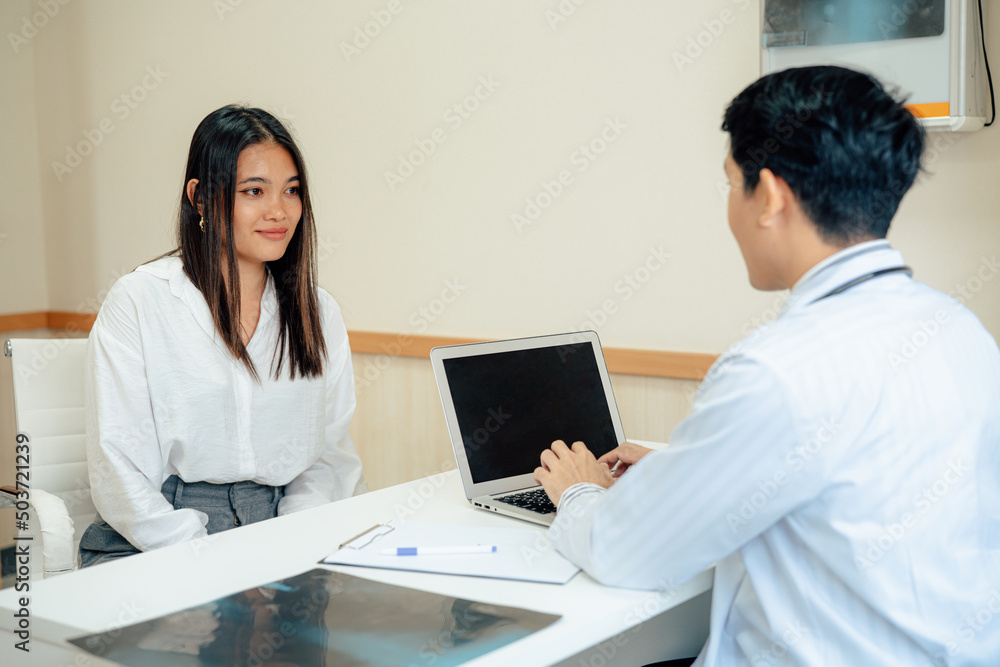 Asian male doctor in white medical uniform consult female patient on consultation. They Consult Digital Tablet Computer while Talking about Patient's Health. Asian male doctor in white medical uniform consult female patient on consultation. They Consult Digital Tablet Computer while Talking about Patient's Health.