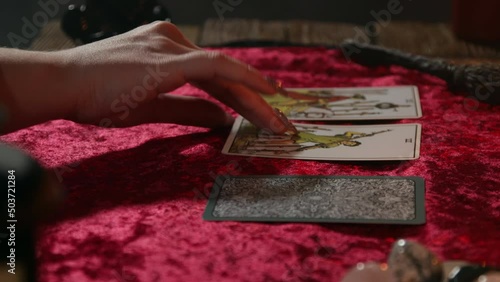 The fortune teller's hand turns over three tarot cards lying on a burgundy tablecloth. photo