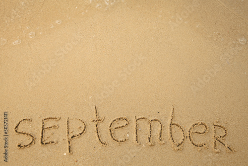 September - handwritten on the soft beach sand with a soft lapping wave.