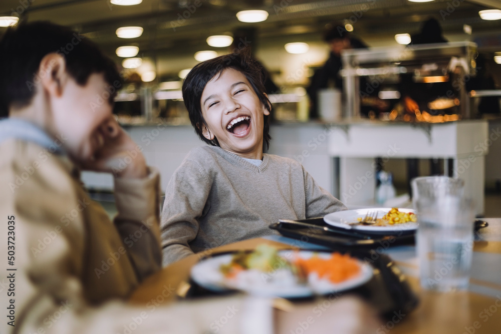 Boy laughing while sitting with friend during lunch break at school Boy laughing while sitting with friend during lunch break at school