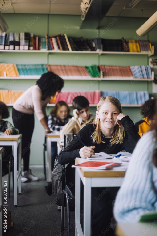 Smiling girl leaning on elbows while sitting at desk in classroom Smiling girl leaning on elbows while sitting at desk in classroom