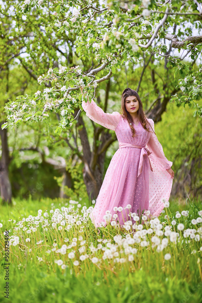 a young woman in a pink dress posing next to a blossoming apple, spring portrait. a young woman in a pink dress posing next to a blossoming apple, spring portrait.