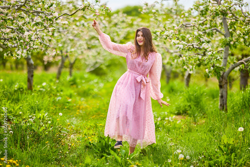 a young woman in a pink dress posing next to a blossoming apple, spring portrait. a young woman in a pink dress posing next to a blossoming apple, spring portrait.