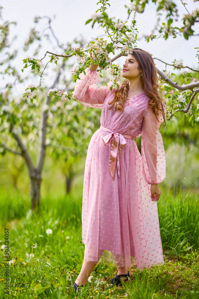a young woman in a pink dress posing next to a blossoming apple, spring portrait. a young woman in a pink dress posing next to a blossoming apple, spring portrait.
