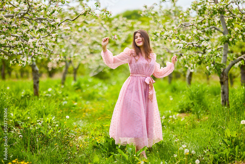 a young woman in a pink dress posing next to a blossoming apple, spring portrait.