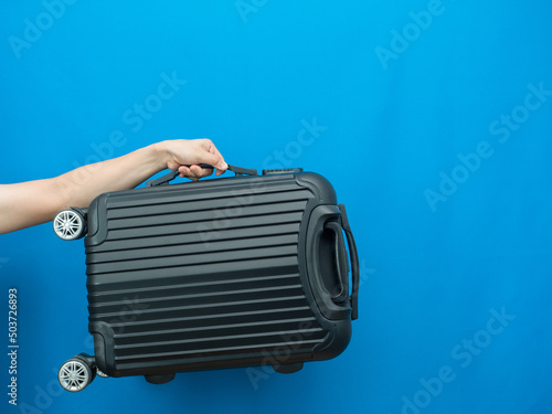 Man hand holding luggage on blue background holiday concept