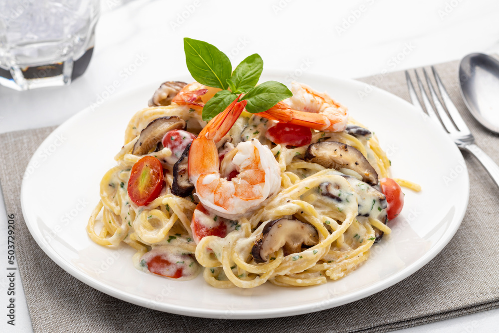 Spaghetti with creamy white sauce, shrimps and mushrooms served on a white serving plate and garnish with fresh Italian sweet basil leaves. Spaghetti with creamy white sauce, shrimps and mushrooms served on a white serving plate and garnish with fresh Italian sweet basil leaves.