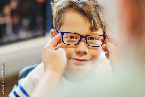 Valokuva ophthalmologist trying eyeglasses on smiling boy in optics store, banner
