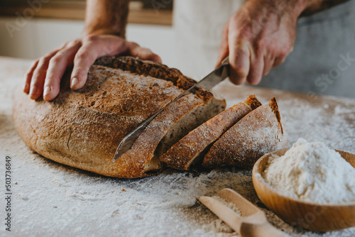 Fototapeta Young man in apron cutting homemade bread