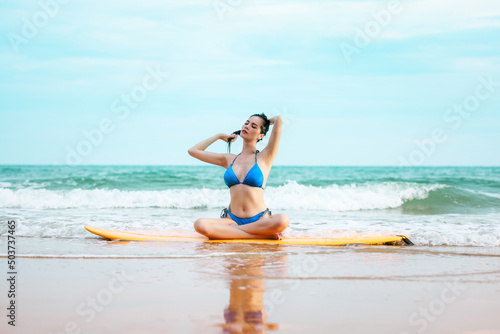 beautifull asian girl wearing bikini siting on surfboard and poses at the sand beach  in a tropical location 