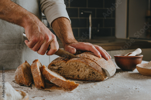 Foto Young man in apron cutting homemade bread