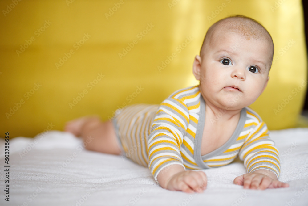 Adorable baby in sunny bedroom. Newborn baby is resting in bed with a warm soft blanket. Family morning at home. Smiling child looking at camera.