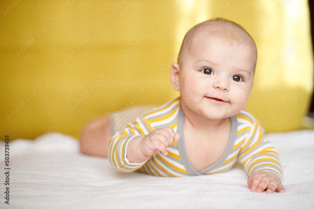 Adorable baby in sunny bedroom. Newborn baby is resting in bed with a warm soft blanket. Family morning at home. Smiling child looking at camera. Adorable baby in sunny bedroom. Newborn baby is resting in bed with a warm soft blanket. Family morning at home. Smiling child looking at camera.
