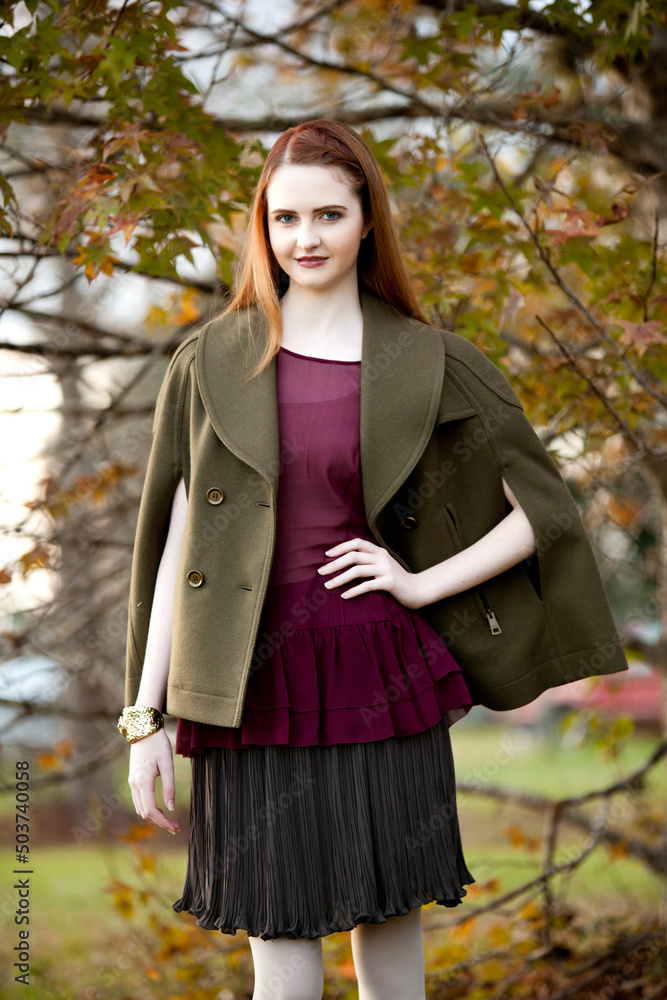 Beautiful Young Female Fashion Model with Red Hair Posing in Jewel Tone Fall Clothing Standing Outside with Autumn Leaves and Trees Beautiful Young Female Fashion Model with Red Hair Posing in Jewel Tone Fall Clothing Standing Outside with Autumn Leaves and Trees
