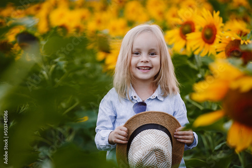 Little girl six years old in a hat poses for the camera in a field of sunflowers and holds a bouquet in her hands