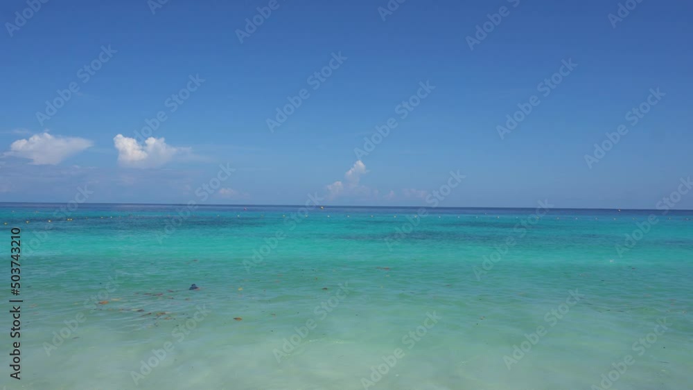 Turquoise ocean water. Leaves are floating. In the distance, buoys with a net against dangerous marine fish and jellyfish. White clouds, blue sky. The water shimmers from blue to dark blue. Similans Turquoise ocean water. Leaves are floating. In the distance, buoys with a net against dangerous marine fish and jellyfish. White clouds, blue sky. The water shimmers from blue to dark blue. Similans
