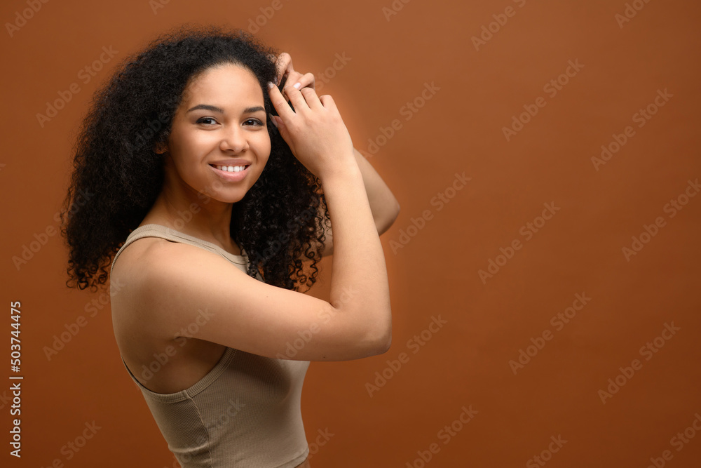 Studio portrait on the brown background of carefree serene multiracial woman looking at camera and laughs. Cheerful peaceful african lady typify self love and body care, charming 20s female Studio portrait on the brown background of carefree serene multiracial woman looking at camera and laughs. Cheerful peaceful african lady typify self love and body care, charming 20s female