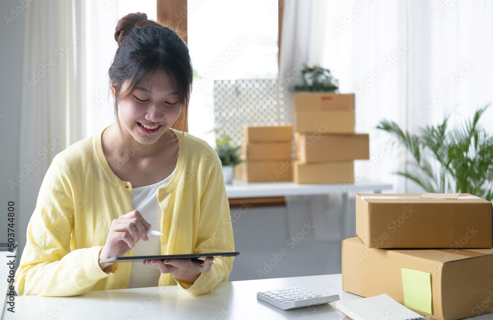 Portrait business Asian woman smile and use tablet checking information on parcel shipping box before send to customer. Entrepreneur small business working at home. SME business online marketing. Portrait business Asian woman smile and use tablet checking information on parcel shipping box before send to customer. Entrepreneur small business working at home. SME business online marketing.