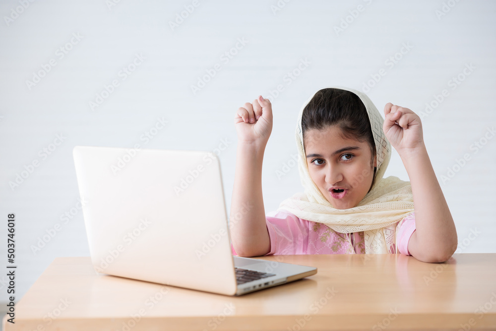 muslim girl using a laptop computer and raised hand for celebrating good news on the table muslim girl using a laptop computer and raised hand for celebrating good news on the table
