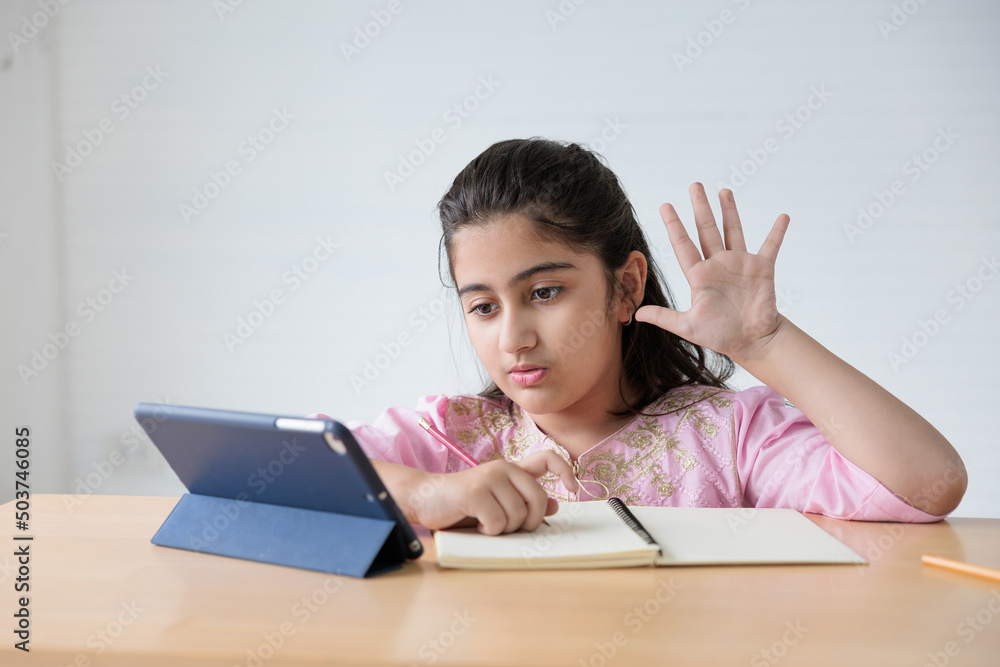 cute Indian girl video call to someone, pointing pose or number one finger sign and looking tablet for online learning class, education concept cute Indian girl video call to someone, pointing pose or number one finger sign and looking tablet for online learning class, education concept