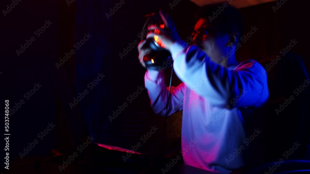 Man with headphones loses an online game on laptop and irritably removes headphones from head, side view. Man loses videogame on laptop, rips headset off his head Man with headphones loses an online game on laptop and irritably removes headphones from head, side view. Man loses videogame on laptop, rips headset off his head