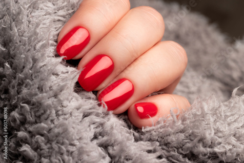 Female hand with beautiful manicure - red nails on gray fluffy knitted fabric. Nail care concept