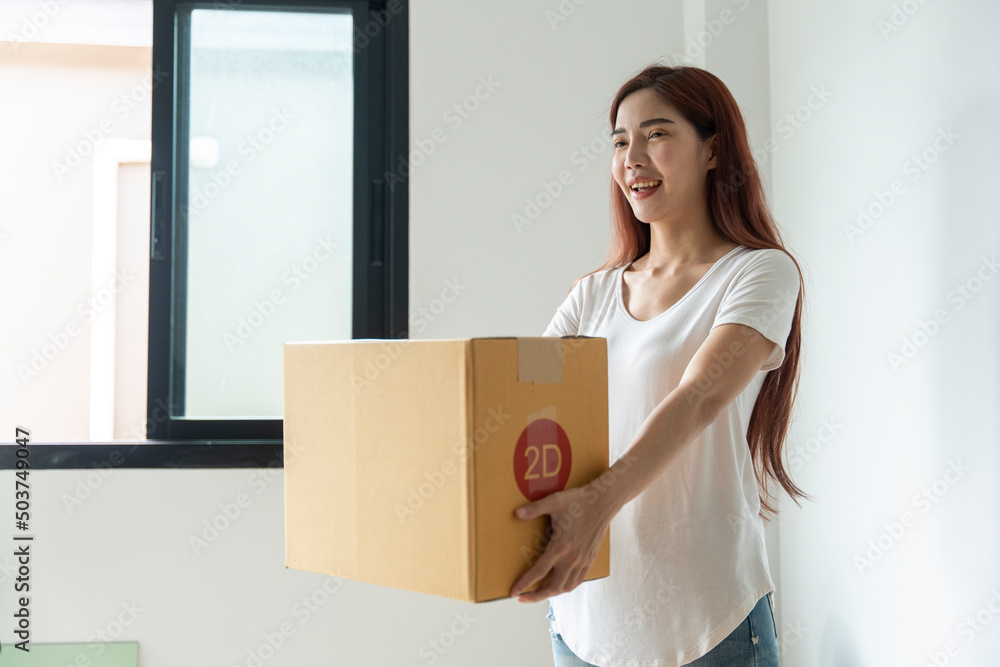 Asian woman packing boxes to move house which they live happily holding a big box.