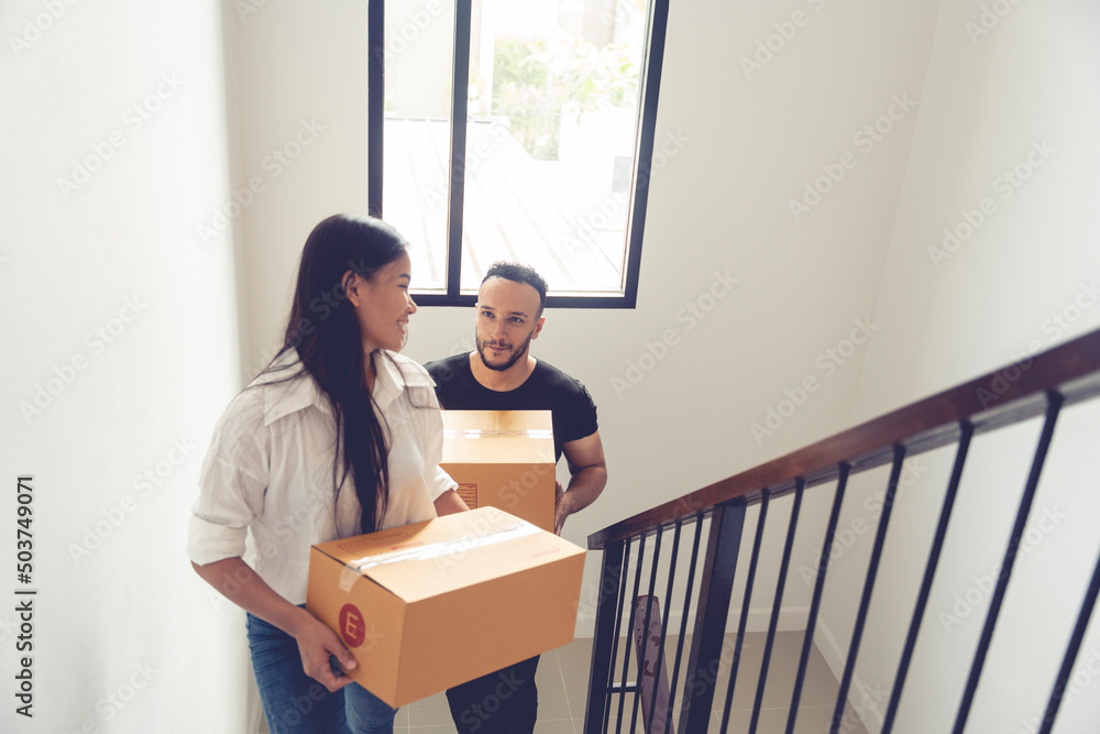 Thai and Caucasian couple holding boxes of things walk up stairs to move into a new home with fun Thai and Caucasian couple holding boxes of things walk up stairs to move into a new home with fun