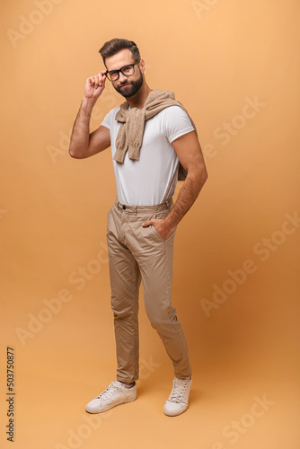 Full length view of the caucasian positive stylish man wearing glasses going somewhere isolated on orange background. Indoor studio shot photo