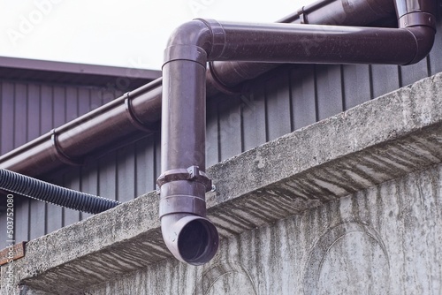 brown plastic drainpipe on the wall above the gray concrete fence outside
