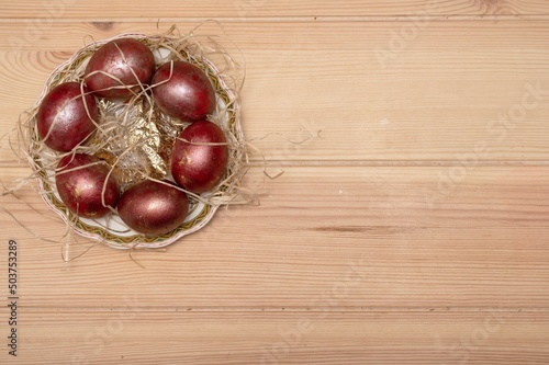 Festively painted in classic red, Easter eggs lie on a straw-covered porcelain saucer.