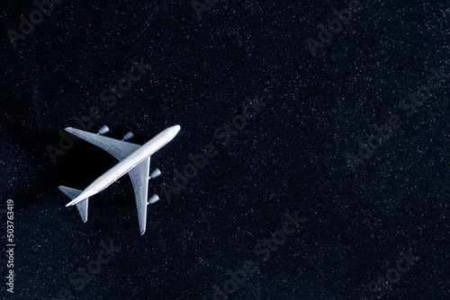 Toy airliner on a silvery dark blue background imitating the night sky. Concept of a romantic night flight among the stars. Travel and relocation. Diagonal. Copy space