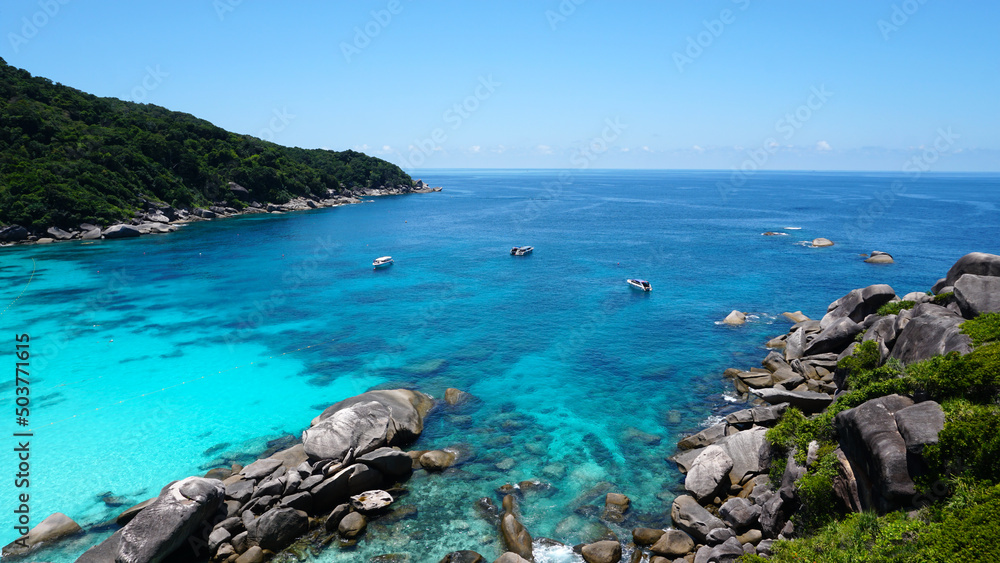Turquoise water in the bay. View of the island and the sea. High cliffs covered with green trees. The gradient of water from blue to blue. There are speedboats, people swim in places. Similan Islands Turquoise water in the bay. View of the island and the sea. High cliffs covered with green trees. The gradient of water from blue to blue. There are speedboats, people swim in places. Similan Islands