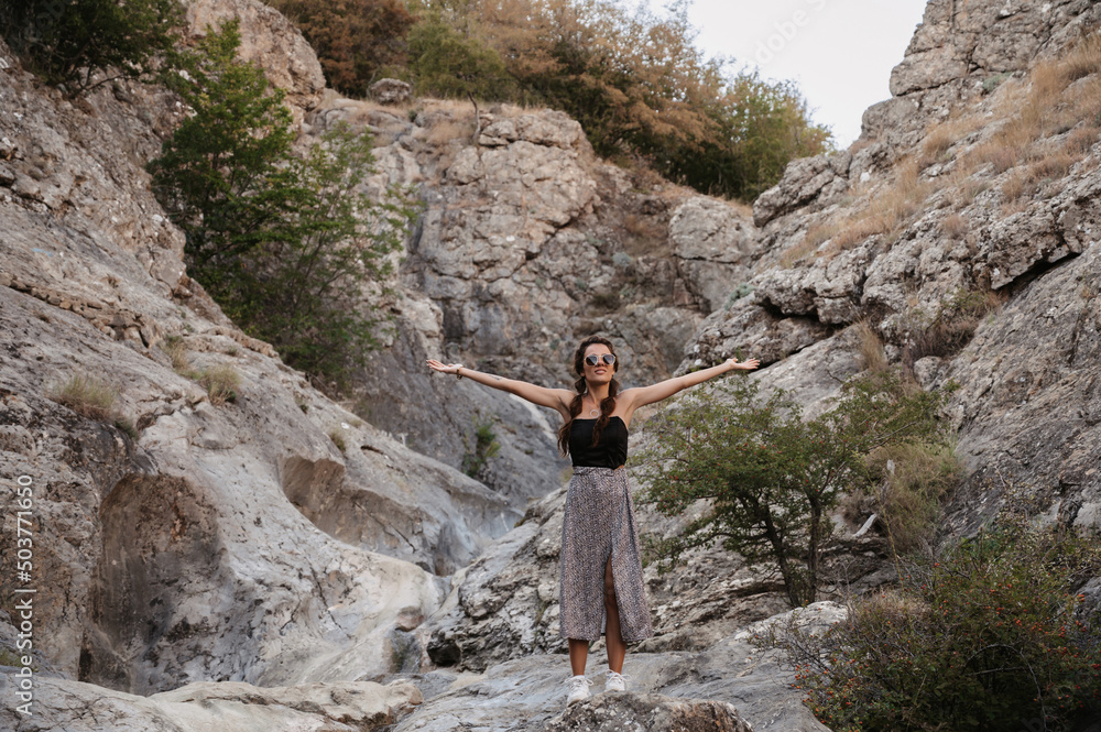 A young woman stands with her hands up in the fresh air in a mountainous area. A smiling woman greets the sun.