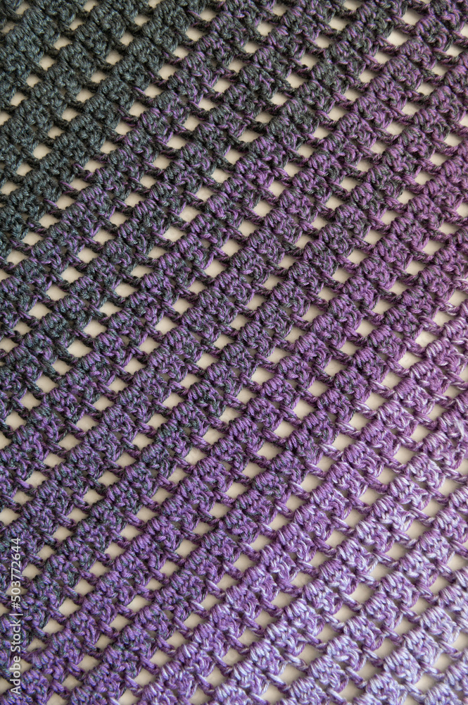 Crochet product from multicolored threads. Handmade backdrop. Flat lay. Fragment of a baktus of violet or puple and grey tone. Striped and geometric pattern