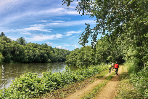 On a sunny summer day, a small group of cyclists ride a trail through a lush green woods beside a quiet river. in Wisconsin.