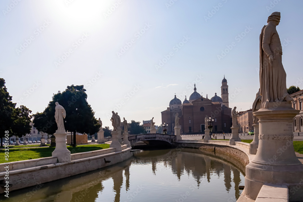 Scenic view on Prato della Valle, square in the city of Padua, Veneto, Italy, Europe. Green island at center, Isola Memmia surrounded by canal bordered by two rings of statues. Basilica of St Giustina