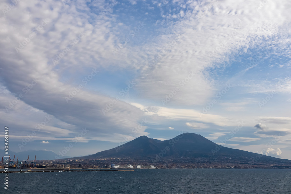 Panoramic view from Castel dell Ovo (Egg Castle) on volcano Mount Vesuvius in Naples, Campania, Italy, Europe. Ferries in the port of Naples. Clouds are accumulating around the mountains. Sea view