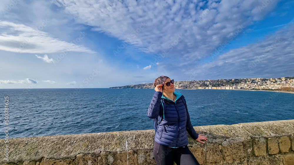 A tourist woman enjoying the panoramic view from Castel dell Ovo (Egg Castle) on the city of Naples, Campania, Italy, Europe. Person leaning against the castle wall, bathing in the sun. Sea view A tourist woman enjoying the panoramic view from Castel dell Ovo (Egg Castle) on the city of Naples, Campania, Italy, Europe. Person leaning against the castle wall, bathing in the sun. Sea view