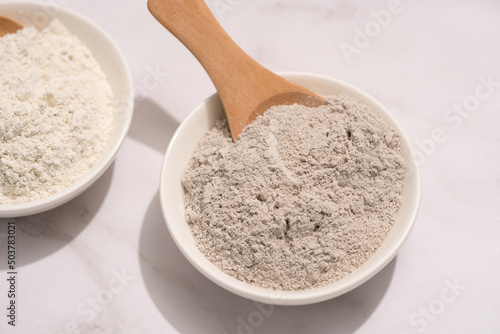 Closeup view of gray and white cosmetic clay on white marble table - mineral powder, bentonite facial mask. Skincare beauty concept. Top view photo