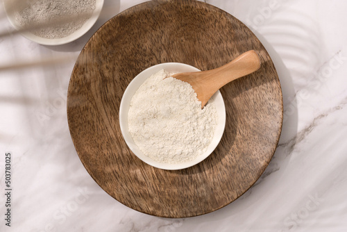 Top view on bowl with white cosmetic clay on wooden tray - mineral powder, bentonite facial mask, kaolin. Skincare beauty concept. Top view