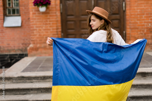 Beautiful girl standing in Ukrainian flag worried about war. Cute woman is feeling emotional pain after reading the news. Freedom and patriot of Ukraine.. Pray for Ukraine. Love Ukraine concept.