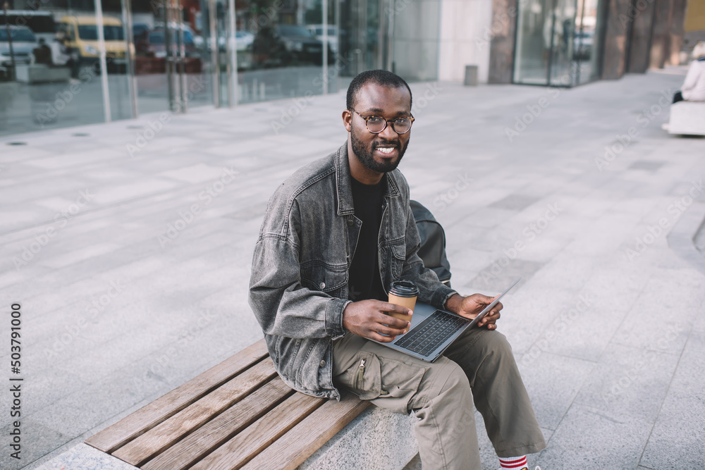 Obraz premium Portrait of happy digital nomad smiling at camera during time for remote working on computer, cheerful millennial male blogger with modern laptop technology posing while doing freelance distance job