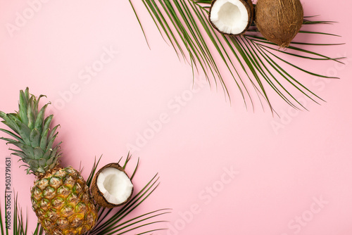 Summer concept. Top view photo of tropical fruits coconuts pineapple and palm leaves on isolated pastel pink background with copyspace