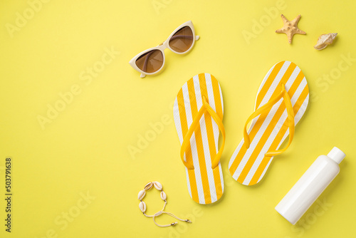 Summer rest concept. Top view photo of yellow striped flip-flops sunglasses sunscreen bottle shell bracelet and starfish on isolated yellow background with copyspace photo