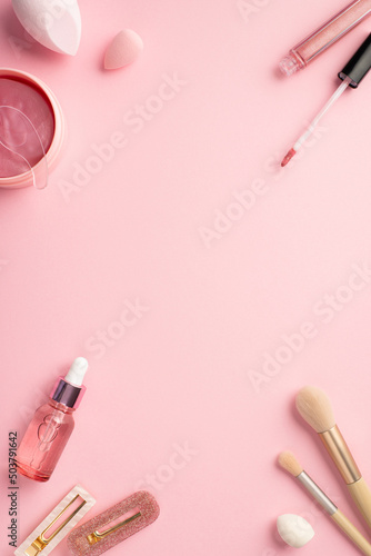 Top view vertical photo of beauty blenders pink eye patches with special spoon lip gloss glass dropper bottle makeup brushes and two stylish hairpins on pastel pink background with blank space
