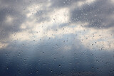 Raindrops on window glass on blurred background of sky with storm clouds. Beautiful water drops, rainy weather with sunbeams