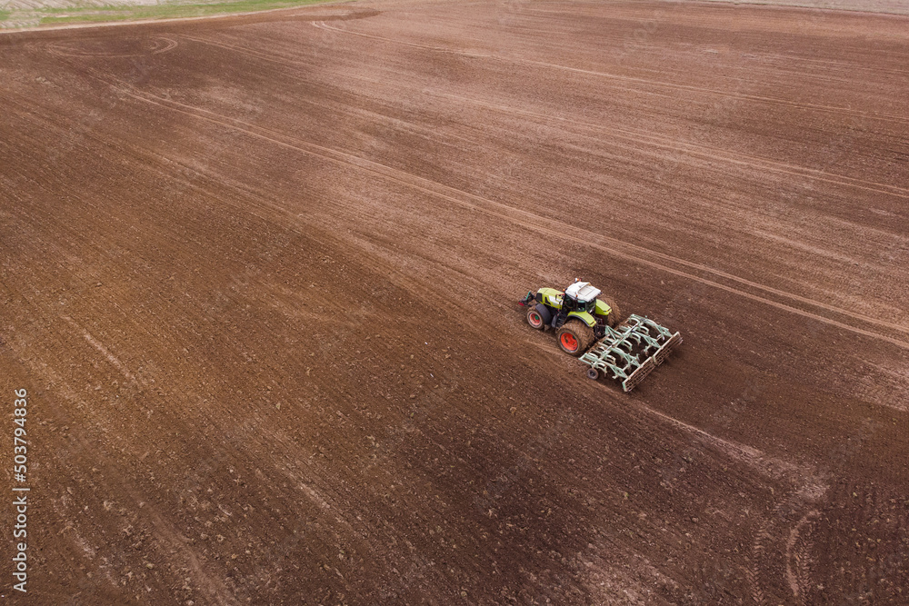 Fototapeta premium A tractor with a disc harrow plows a field for sowing crops. Aerial photography.