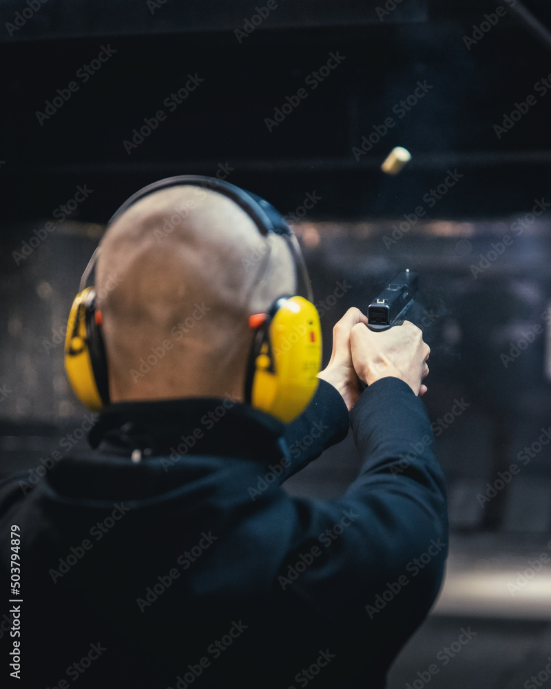 A bald man shooting a 17 pistol in a shooting range. A shellcase